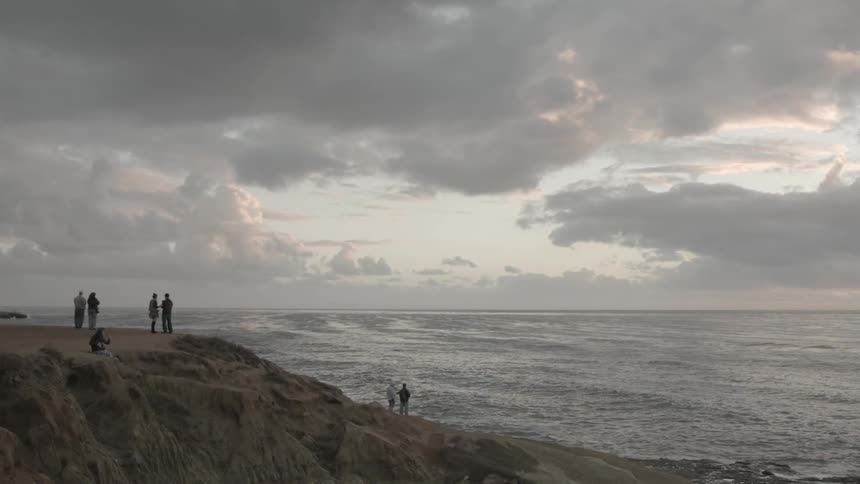 A group of people stand near the ocean on an overcast day