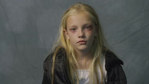 Girl with puffy eyes blinking in front of a gray background