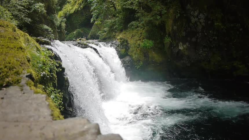 A waterfall flows near a grassy mountainside