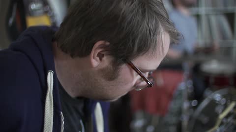 A man plays a guitar with a drummer in the background