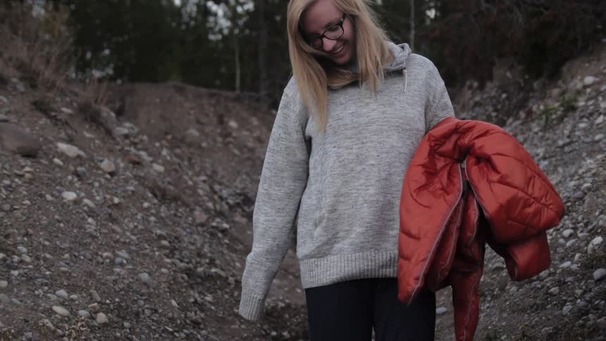 A woman, carrying a jacket, walks in a rocky place