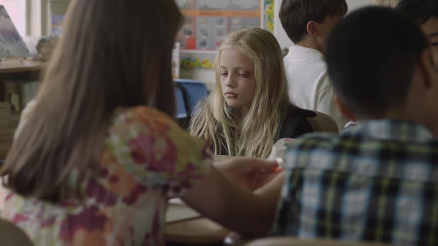 A blonde girl tilting her head back and rolling her eyes while sitting in a classroom