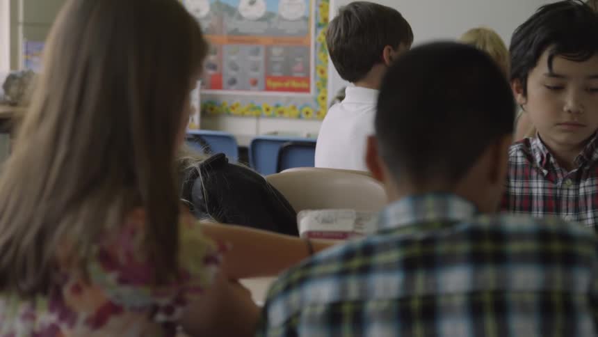 A girl with a bruised face sits at a table with classmates