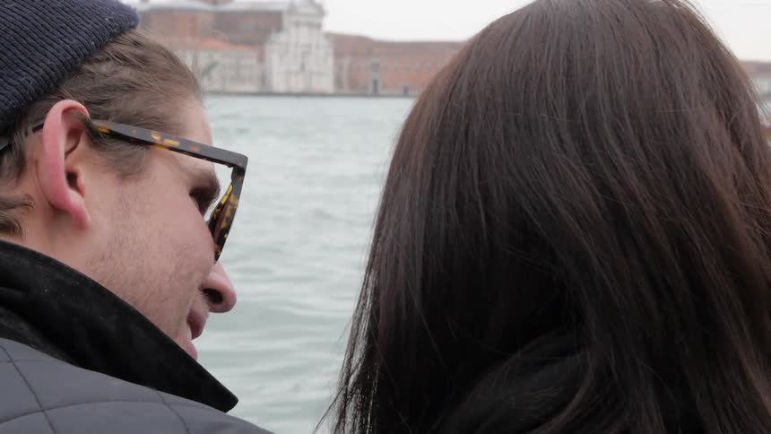 A man and woman talking in front of a boat and water