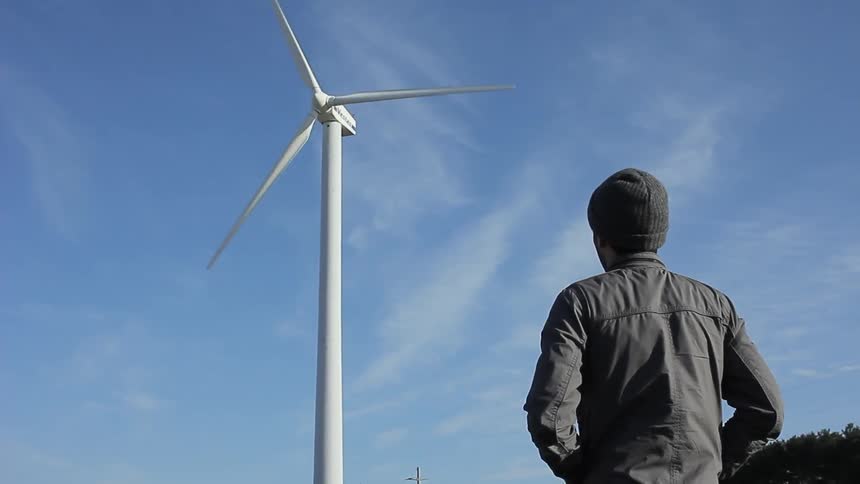 Man standing outside looking up to a wind turbine on a cloudy day