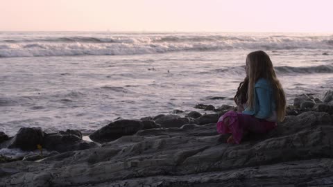 A young girl sits on a rock by the ocean