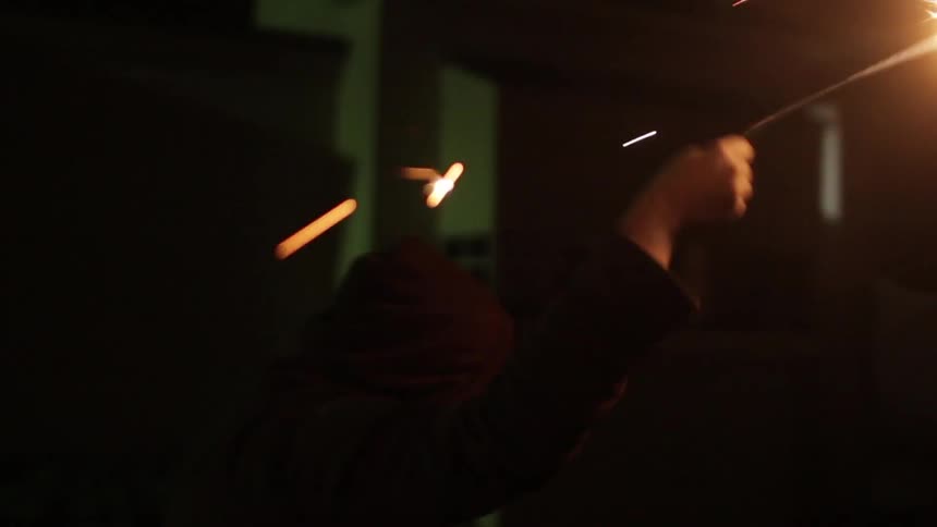 A person waves a burning sparkler above their head at night