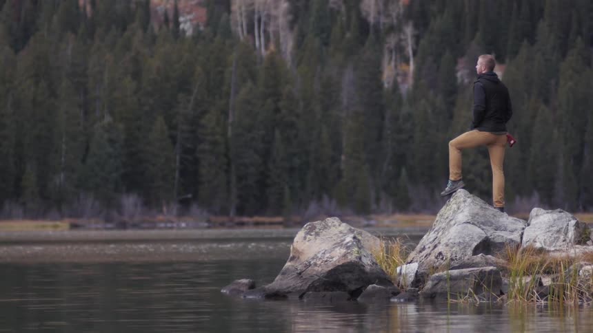 A man stands on a rock near a lake