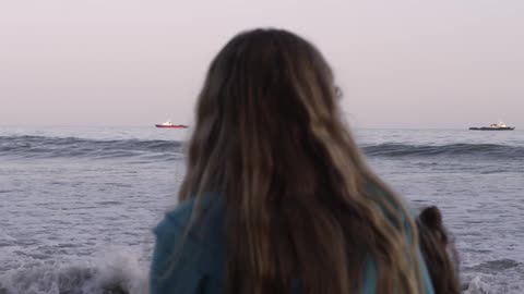 A girl looks towards ships floating on the ocean