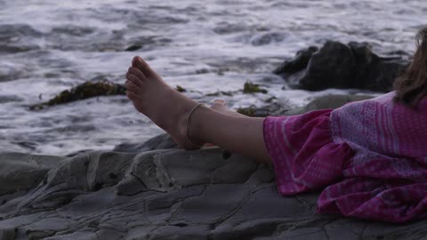 Girl lays on rocks with feet facing water