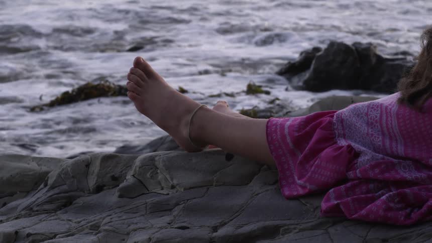 Girl lays on rocks with feet facing water