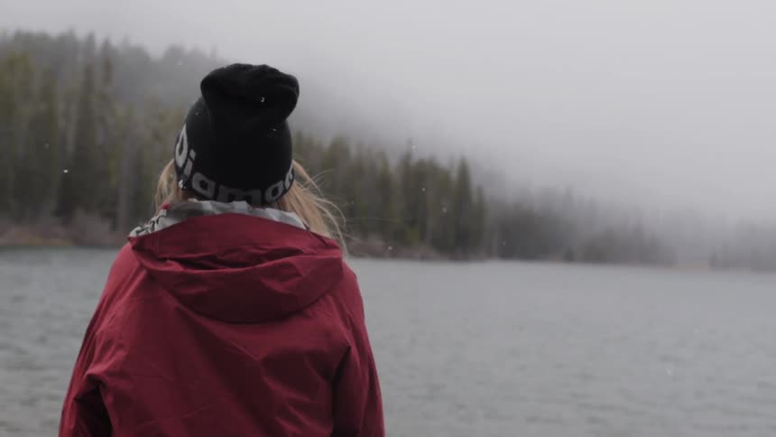 A woman standing outside watching a lake as it snows