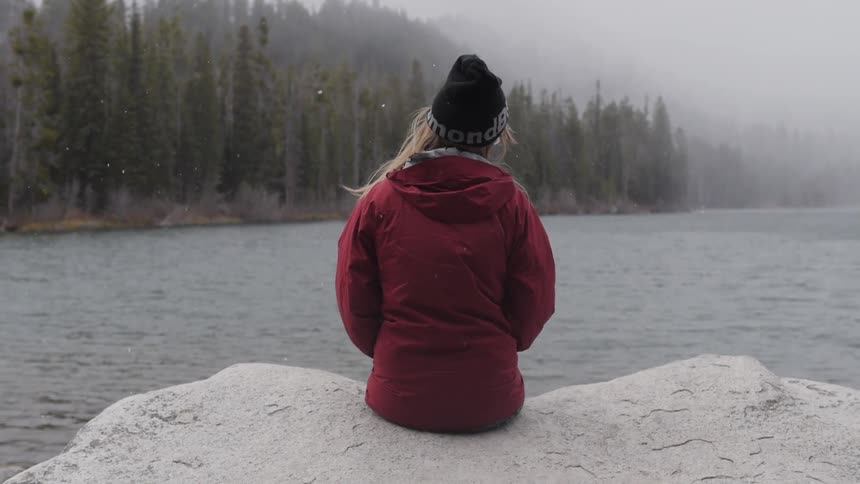 A woman sits on a rock near a lake