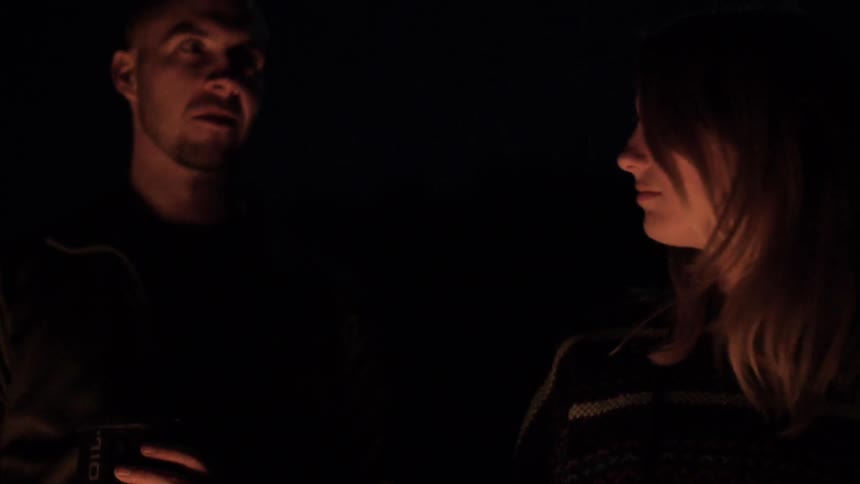 Man and woman sitting in the dark by a campfire