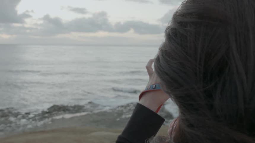A woman taking a picture of the beach during the day