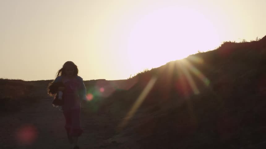 Girl running down a hill as the sun sets behind her