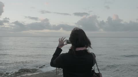 A woman uses an iphone to take a picture near the beach