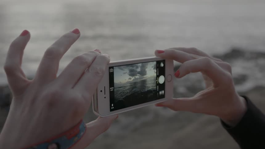 Woman takes a photograph of the ocean with a smartphone
