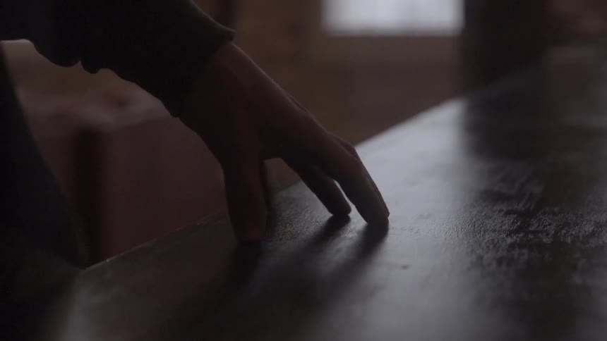 Man sliding his hands along a wooden table in a dark room