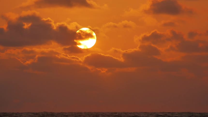 The sun behind the clouds in an orange sky