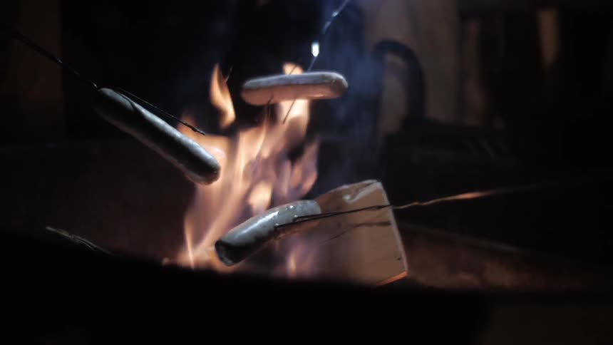 People roasting hot dogs on a lit fire at night