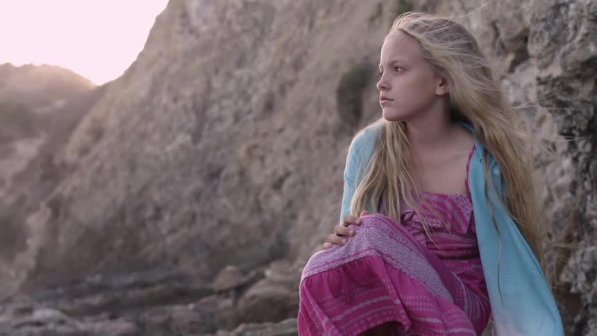 Girl sitting by rocks staring forward on a cloudy day
