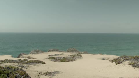 A first person view of walking towards the edge of a sandy cliff next to the water