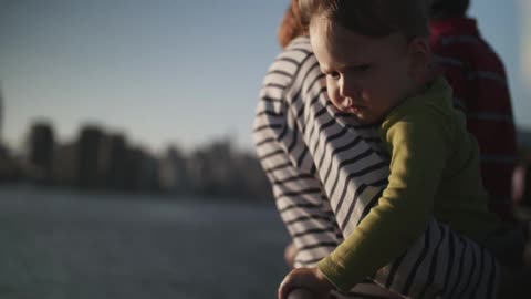A woman holding a toddler in her arms as she leans back against a railing