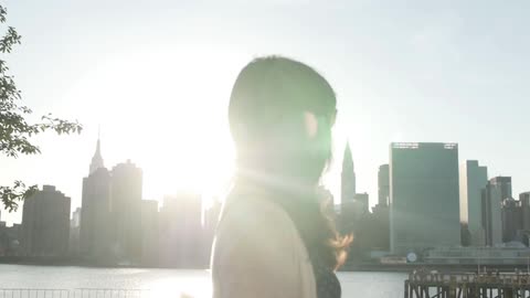 Woman walks beside river with city skyline in background