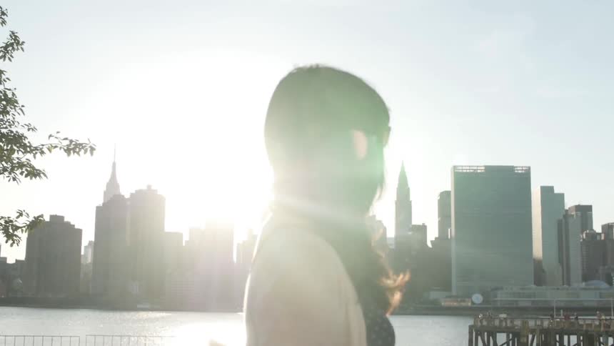 Woman walks beside river with city skyline in background