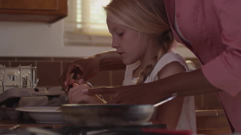 A woman helps a girl with cooking in the kitchen