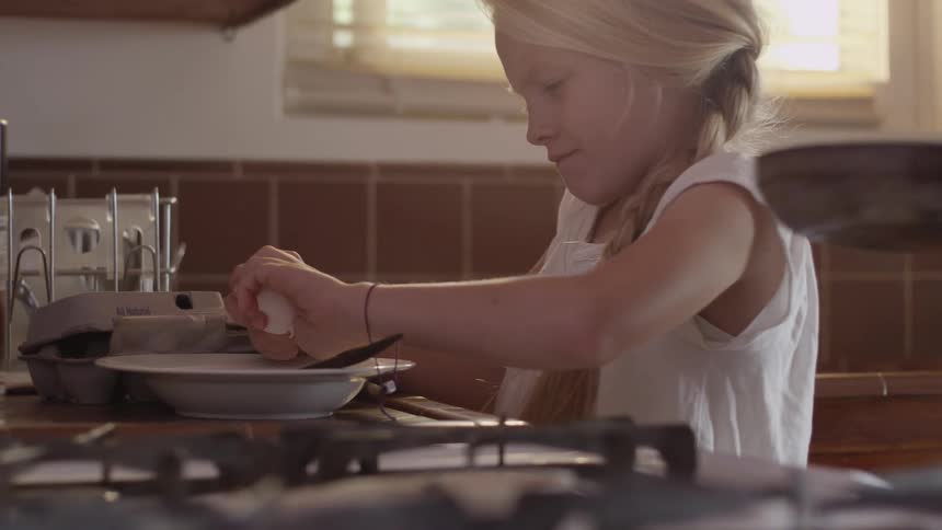 A girl cracks an egg into a bowl