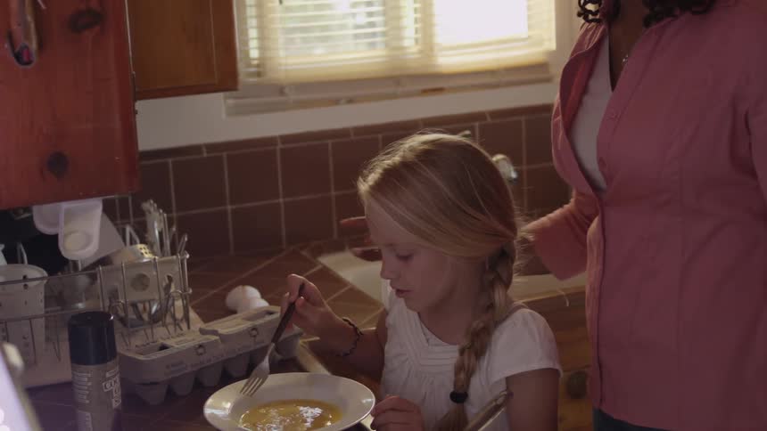 Woman helping a young girl cook eggs