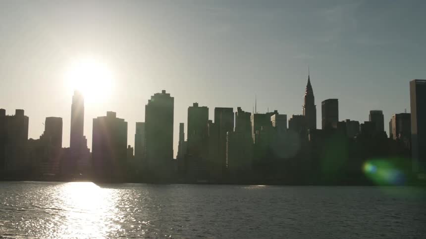 The bright sun is behind a city skyline beside a river