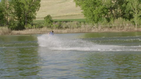 A man wakeboards on a lake and jumps into the air