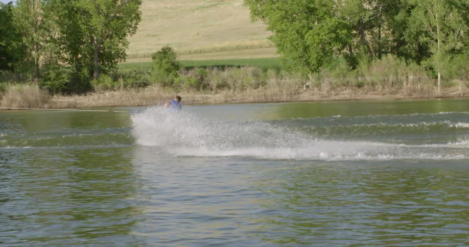 A man wakeboards on a lake and jumps into the air