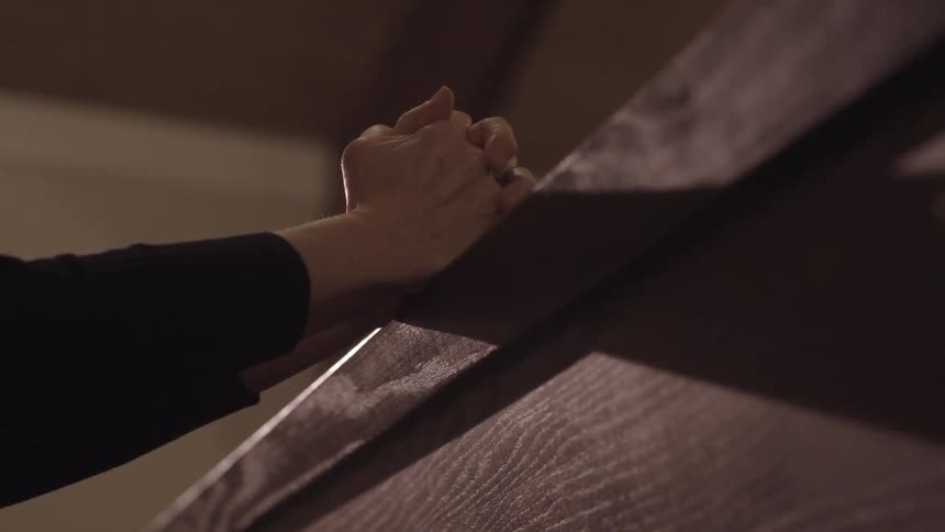 A person folding their hands on a pew