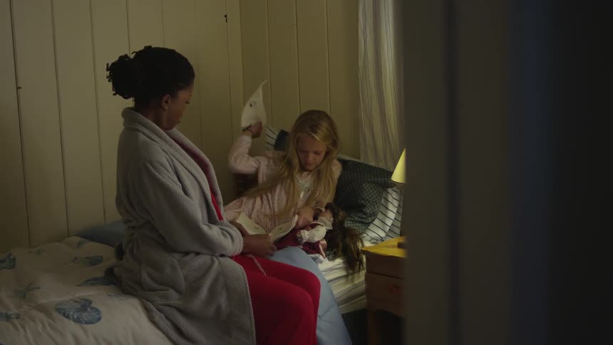 A woman sitting on a bed as a girl lays ripping pages out of a book