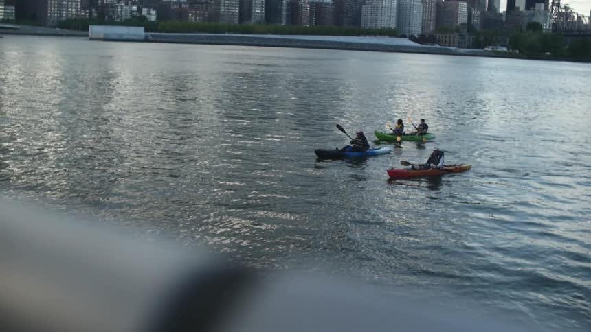 Kayakers paddling down a body of water with buildings along the shoreline