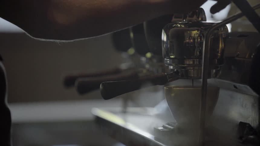 A barista operating an espresso machine and filling a coffee cup