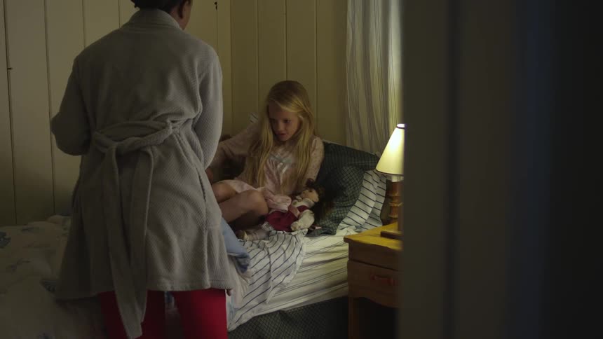 A woman tucks a girl into bed at night