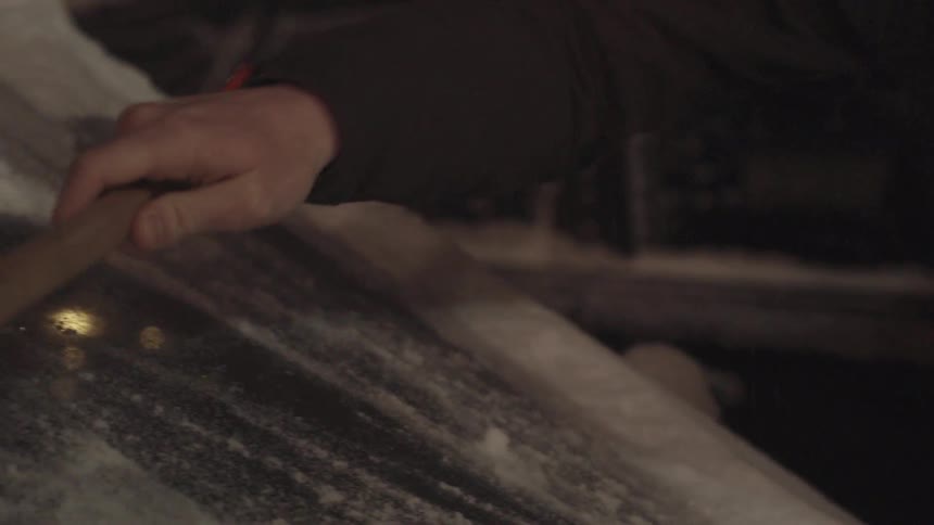 Person brushing the snow off of a car windshield at night