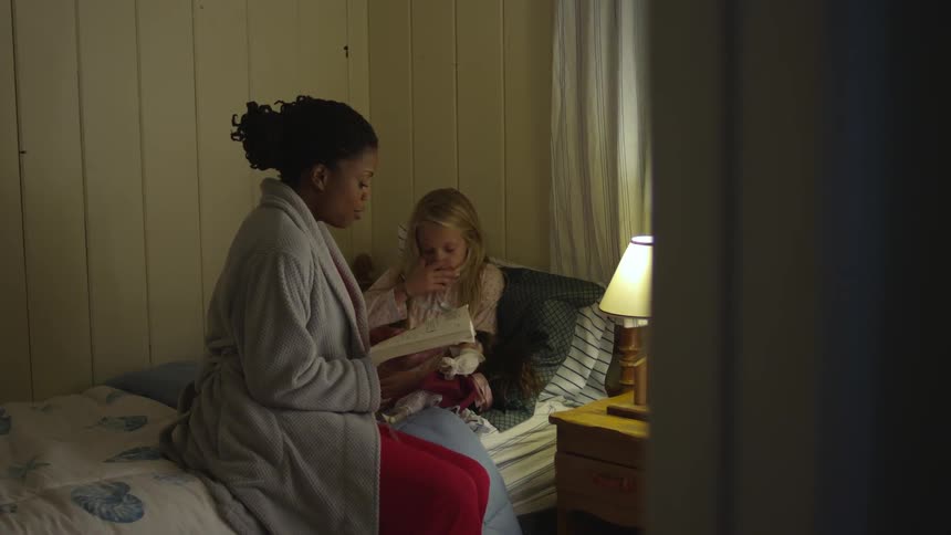 A woman reads to a young girl lying in bed