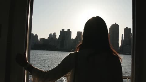 Woman wearing sunglasses looks at city skyline from a yatch
