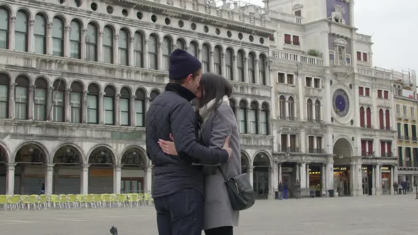 A couple hug in front of an architectural building