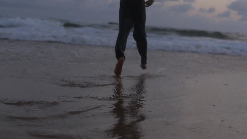 A black child skips along in the sand of a beach at dusk