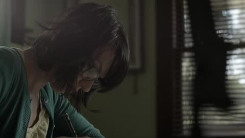 Spectacled woman writing with a pencil wearing a green sweater indoors