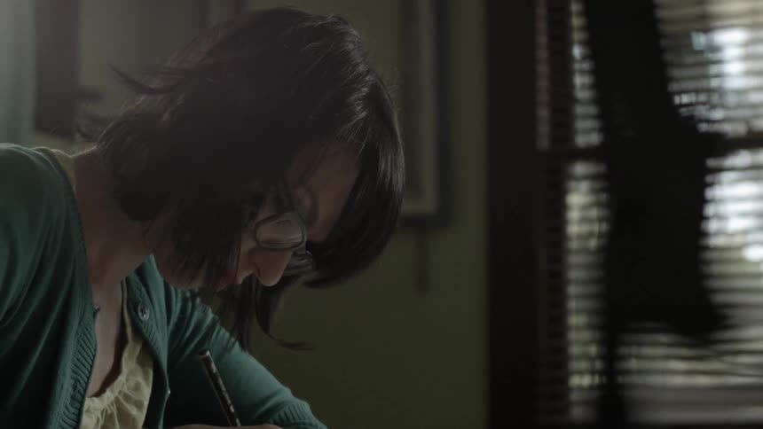 Spectacled woman writing with a pencil wearing a green sweater indoors