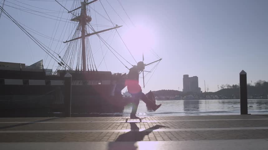 Skateboarding past a docked sailing ship and water