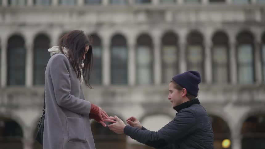 Man proposing marriage to a woman in front of a building